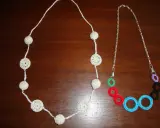 Dos collares de ganchillo y abalorios: uno blanco con esferas y círculos calados, y otro con cadena plateada y aros de colores.
