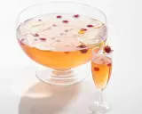 Un grand bol de punch rose avec des tranches de citron et des framboises, prêt pour une recette de soupe champenoise.