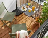 Idéal pour aménager un petit balcon en longueur : deux chaises pliantes vertes, une table avec fruits et jus, et des plantes.