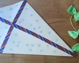 Ein selbstgebastelter Drachen mit Schneeflocken und bunten Bändern, perfekt für basteln mit Kindern ab 7 Jahre. Daneben eine Schnur mit grünen Schleifen und Holzperlen.