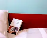 Un libro aperto, "La camera azzurra" di Simenon, giace su un letto bianco, pronto per essere letto.