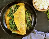 Omlet z serka wiejskiego z zielonymi warzywami na patelni. Obok miseczka z serkiem i natka pietruszki.