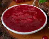 Eine Schüssel mit leuchtend roter Cumberland Sauce, umgeben von frischen Johannisbeeren und grünen Blättern.