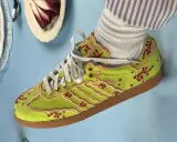 Jaskrawozielone buty Adidas z haftowanymi kwiatami wiśni i różowymi lamówkami, prawdopodobnie najdroższe buty Adidas, prezentowane na błękitnym tle.