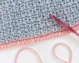 Detalle de tejido a crochet con punto cangrejo en rosa y gris. Una aguja rosa está lista para continuar el trabajo.
