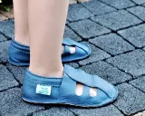 Niebieskie skórzane kapcie dziecięce z otworami na palce na tle kostki brukowej.