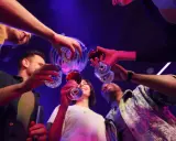 Grupa przyjaciół wznosi toast, świętując weekend. W tle dyskotekowe światła, sugerujące zabawę i być może początek weekendowego alkoholizmu.