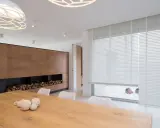 Un salon moderne avec un grand mur en bois, une table en bois et un type de store vénitien blanc qui habille une large fenêtre.
