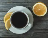 Eine Tasse schwarzer Kaffee mit Zitrone und Zitronenscheiben auf einem Holztisch.
