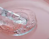 Goutte d'un sérum transparent avec des bulles, sur fond rose. C'est une illustration de ce que sont les peptides, des éléments clés pour la peau.