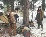 Zimowy obóz bushcraftowy. Dwie osoby w strojach z epoki, namiot, plecaki i sprzęt survivalowy.