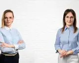 Dwie kobiety w koszulach stoją przed białą ceglaną ścianą.