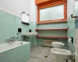 Bad renovieren ohne fliesen abschlagen: hellblau geflieste Wände, Badewanne, Waschbecken, Toilette, Bidet und Fenster.