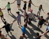 Un grupo de adolescentes participa en juegos cooperativos, tomados de la mano en un círculo en el exterior.