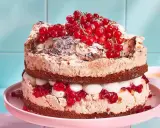 Ein zweistöckiger Johannisbeerkuchen mit Baiser, Sahne und roten Johannisbeeren, bestäubt mit Puderzucker und Mandelsplittern.