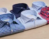 Mehrere gefaltete Hemden in verschiedenen Mustern und Farben liegen auf einem Holztisch. Perfekt zum hemden waschen und Bügeln.
