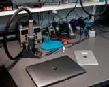 Na biurku serwisowym leży zamknięty laptop, obok tablet. W tle widać stację lutowniczą i narzędzia.