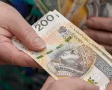 Dwie dłonie przekazują sobie banknot 200 zł. Czy opieka nad dzieckiem niepełnosprawnym wlicza się do emerytury?