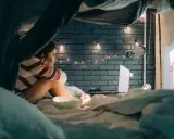 Une jeune femme regarde un écran dans une tente improvisée. Elle se demande combien de temps faut-il arrêter les écrans avant de dormir.