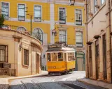 Gelbe Straßenbahn fährt durch enge Gassen Lissabons. Perfekt für angenehme Portugal Temperaturen im Mai.