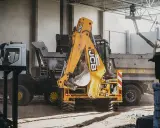 Żółty koparko-ładowarka JCB i ciężarówka na placu budowy.