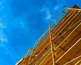 Estructura amarilla de madera y metal, que es una cimbra, contra un cielo azul con nubes finas.
