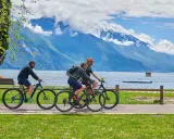 Ciclisti godono di una giornata soleggiata lungo uno dei laghi nord Italia, con montagne maestose sullo sfondo.