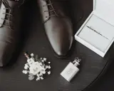 Eleganckie brązowe buty męskie, butonierka, pierścionki w pudełku i piersiówka.