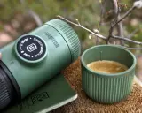 Kawa w górach: nanopresso i filiżanka świeżego espresso na drewnianym pniu, otoczone leśną scenerią.