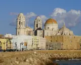 Die Kathedrale von Cadiz, ein majestätisches Bauwerk mit goldenen Kuppeln, ragt über bunte Häuser am Meer auf.