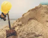 Żółty kask i rękawice na łopacie, obok sterty piachu. Zastanawiasz się, ile waży metr sześcienny piachu?