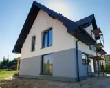 Nowy dom w trakcie budowy, z dwukolorową elewacją i rusztowaniami. Czekamy na wykończenie, by podziwiać efekt końcowy.