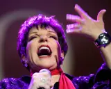 Liza Minnelli, en ikonisk artist, sjunger med passion på scenen, hennes ansikte upplyst av lila ljus.
