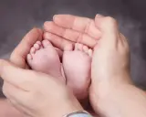 Manos adultas sostienen delicadamente los pies de un bebé. A partir de la semana 37, un bebé puede nacer.