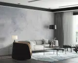 Nowoczesny salon z szarą sofą i fotelem. W tle efektowny **beton na ścianie**, który nadaje wnętrzu industrialnego charakteru.