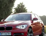 Czerwone BMW 118d na tle drzew i pól.