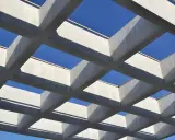 Estructura geométrica de vigas de hormigón armado, creando un patrón de cuadrados contra el cielo azul.