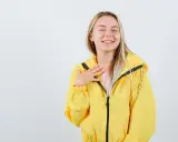 Uśmiechnięta blondynka w żółtej kurtce softshellowej, która przypomina jej, jak prać softshell, by zachować jego właściwości.