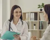 Lekarka w białym kitlu z notatnikiem w ręku, słuchając pacjentki. To może być dokument s1 norwegia.