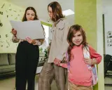 Zwei Frauen besprechen ein Dokument, während ein Mädchen mit Rucksack lächelt. Hoffentlich ist keine Note ungenügend!