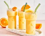 Drei cremige, eisgekühlte Painkiller Cocktails mit Orangenscheiben und grünen Strohhalmen auf einem Terrazzo-Tablett.