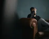 Uomo seduto su un divano di pelle, con la mano sul viso, immerso in pensieri di rimpianto e rimorso.