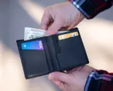 Dłonie wkładają pieniądze i kartę Visa do czarnego portfela.