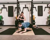 Ein Mann macht einen Unterarmstütz, während eine Trainerin die Zeit stoppt. Perfekt für einen HIIT Trainingsplan im Fitnessstudio.