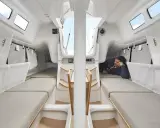 L'intérieur du voilier, premier 27, offre des couchettes confortables et un espace de vie lumineux. Un homme se repose, profitant du calme.