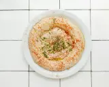Cremiger Hummus-Dip mit Paprikapulver, Pinienkernen und Petersilie auf einem Teller, bereit zum Dippen.