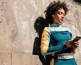 Frau mit Kopfhörern lehnt an Wand, hält handy beim joggen. Musik und Motivation für die Laufstrecke.