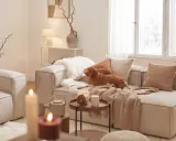 Un chien brun se repose sur un canapé dans un salon cosy. Des coussins douillets, des plaids et des bougies créent une atmosphère chaleureuse.