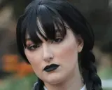 Maquillaje de Miércoles Addams con labios negros y ojos ahumados, peinado con trenzas y flequillo.