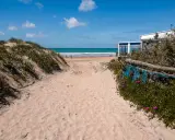 Sandiger Weg zum Conil de la Frontera Strand, mit Dünen, Meer und einem Strandcafé im Hintergrund.